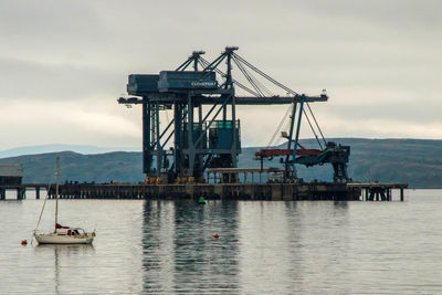 Cranes on pier by sea against sky