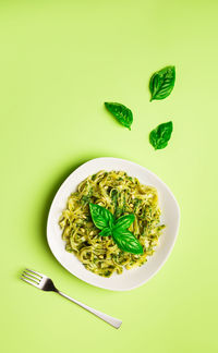 Tagliatelle pasta with pesto sauce, basil and pine nuts on light green background. italian cuisine.