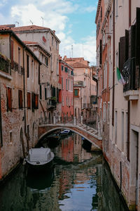 Buildings by canal against sky in city