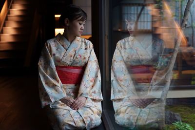 Sad woman wearing traditional clothing looking through window at home