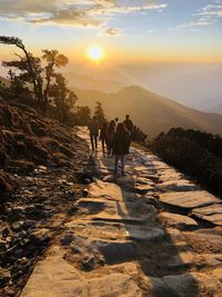 Rear view of people walking on mountain against sky during sunset