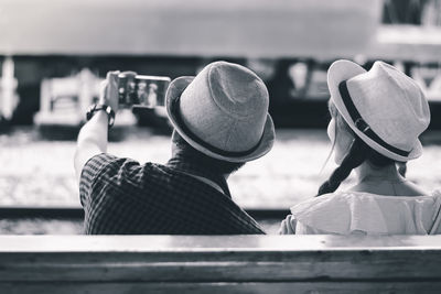 Rear view of couple doing selfie while sitting outdoors