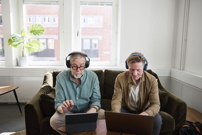 Senior men sitting in living room and using digital tablet and laptop to edit podcast