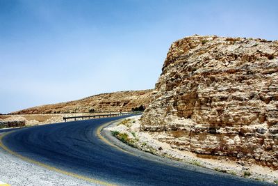 Road by rock formation against clear blue sky