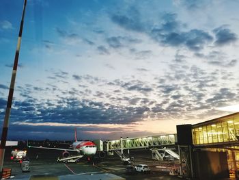 Airplane on airport runway against sky at sunset