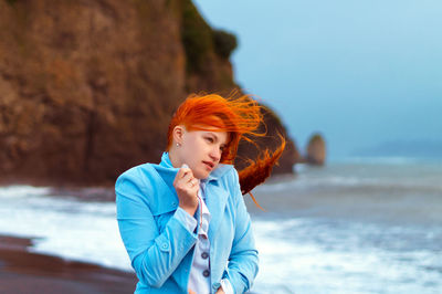 Young woman standing at beach against sky