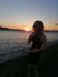 Woman standing at beach against sky during sunset