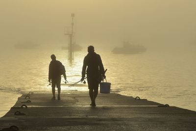 Rear view of men walking on beach against sky