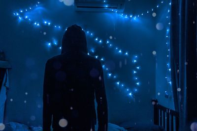 Rear view of silhouette person standing against illuminated string lights