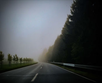 Empty road along trees against clear sky