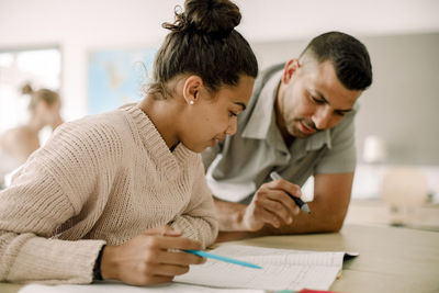 Teenager studying with professor while sitting in classroom