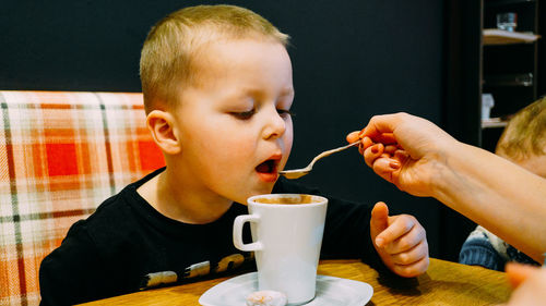 Mother give her son hot drink with a spoon