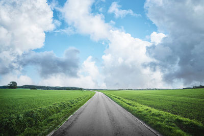 Empty road amidst field against sky