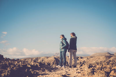 Friends standing on rock against clear blue sky