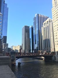 Modern buildings by river against clear sky in city