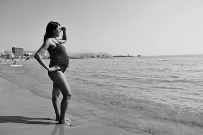 Rear view of young woman standing in sea against clear sky