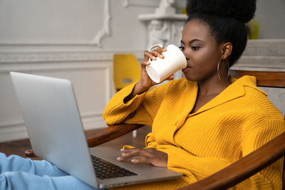 Close-up of smiling woman using laptop sitting on chair at home