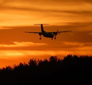 Silhouette airplane flying against sky during sunset