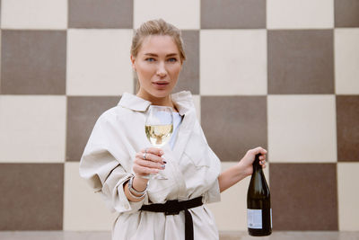Young woman tasting white wine against chessboard background