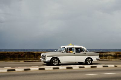 Vintage car on road by sea against sky