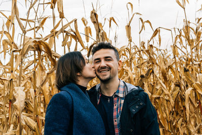 Woman kissing happy smiling man on the cheek standing in autumn in a cornfield