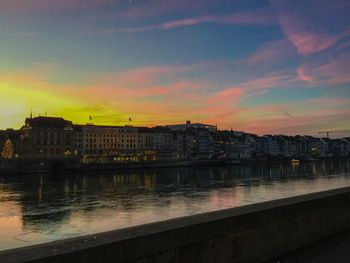 River by illuminated buildings against sky during sunset