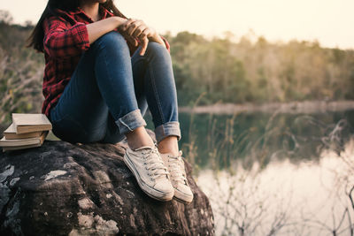 Low section of woman sitting on rock by lake