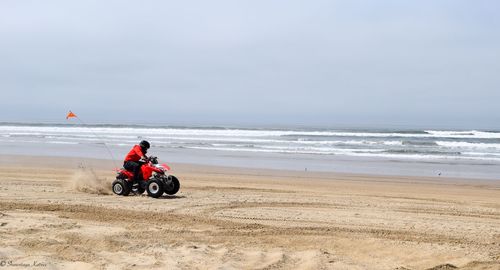 Man riding quadbike at beach against sky