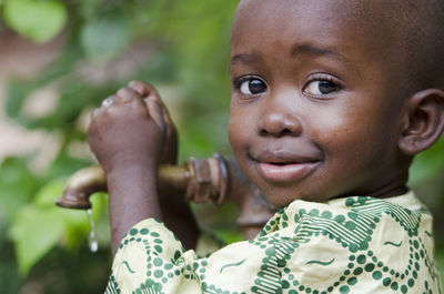 Close-up portrait of cute boy holding faucet against plants