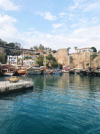 Sailboats in river by buildings against sky