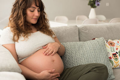 Full length of pregnant mid adult woman sitting on sofa at home