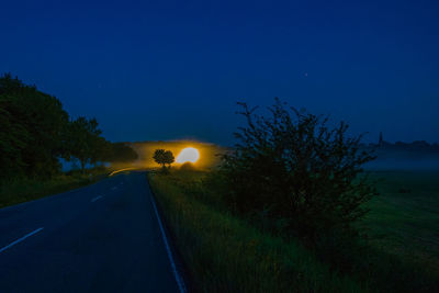 Road amidst trees on field against sky at night