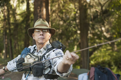 Senior man checking fishing rod in forest