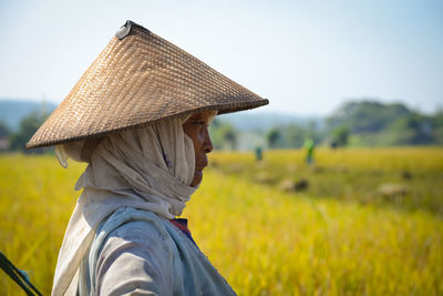 Man wearing asian style conical hat on field against sky