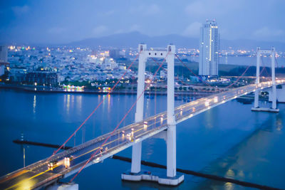 Illuminated bridge over river in city at night