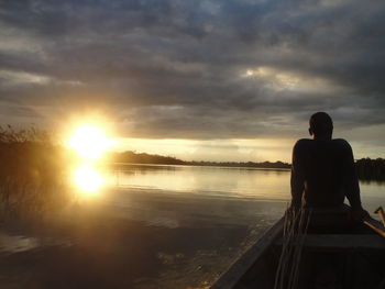 Silhouette man sitting on shore against sky during sunset