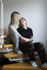 Full length of happy young lesbians sitting on staircase at home