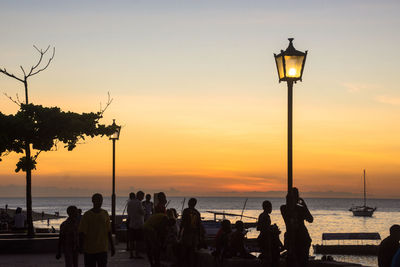 Silhouette people at beach against sky during sunset