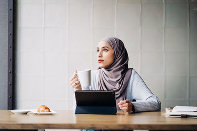 Young woman looking away while sitting on table