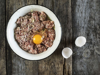 Directly above shot of meat and egg in bowl on wooden table