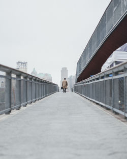 Rear view of man walking on footbridge against clear sky