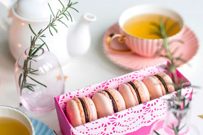 Gift box with pink macaroons among vintage cups of green tea on white background.