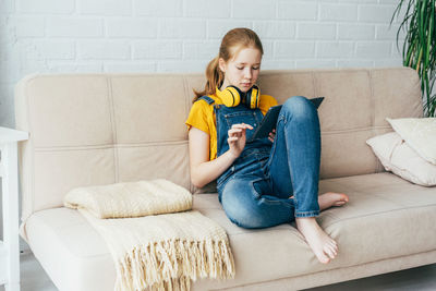 Full length of girl sitting on sofa at home