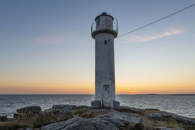 Lighthouse by sea against sky during sunset