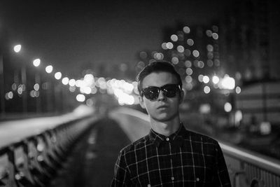 Portrait of young man standing against illuminated light at night