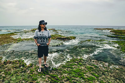 Full length of man standing on rock in sea against sky