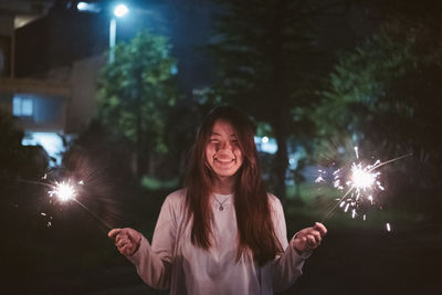 Young woman holding illuminated sparkler while standing at night