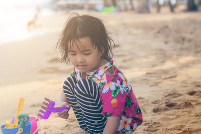 Cute girl playing with toys on sand at beach