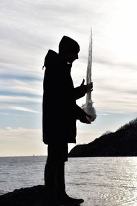 Silhouette man fishing by sea against sky during sunset