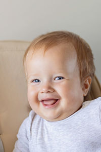 Cute caucasian infant girl ten months old sitting in baby chair and smiling on beige background. 